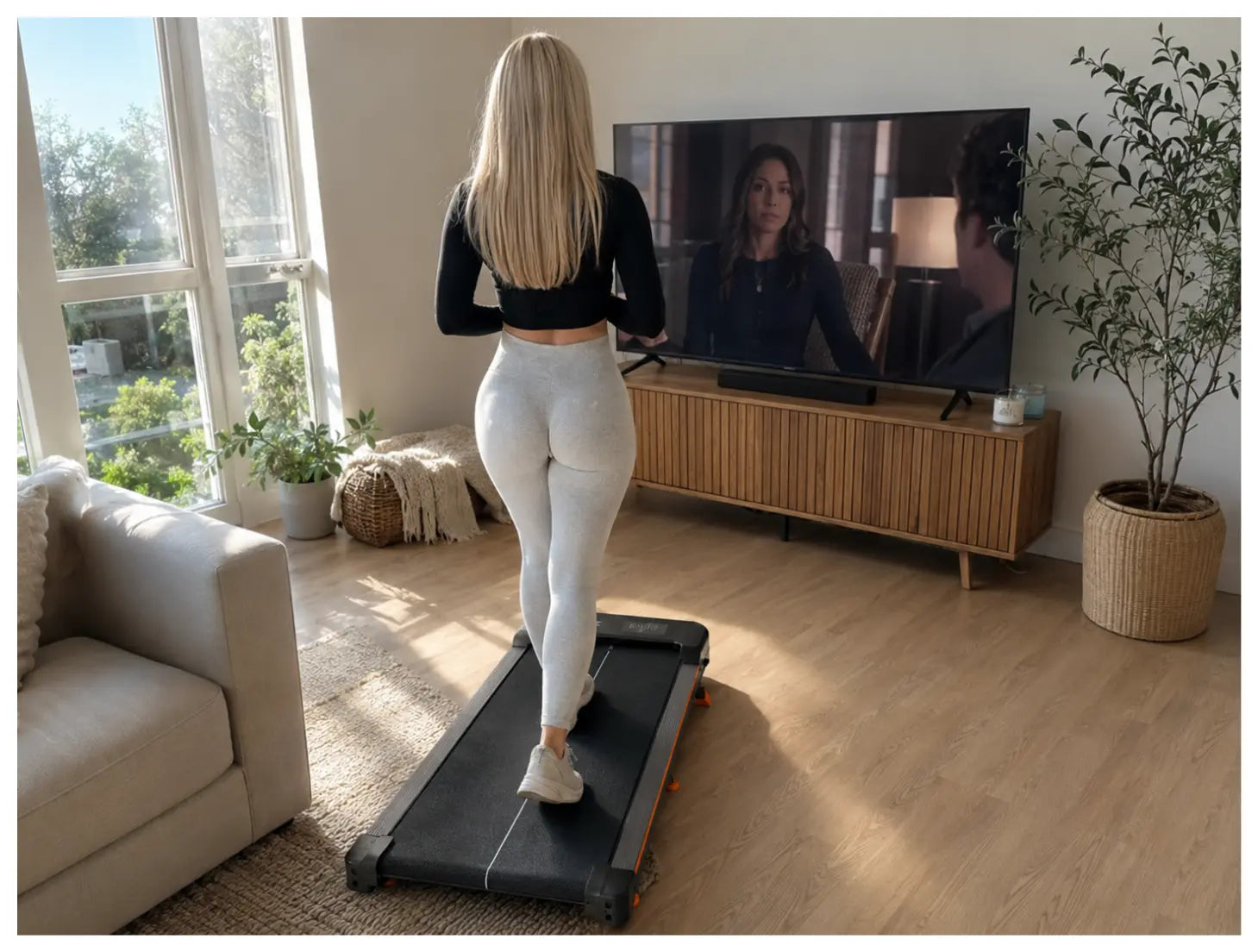 Junge Frau im gemütlichen Hoodie geht barfuß auf dem STRYDE Walking Pad in einem Berliner Wohnzimmer, im Hintergrund ein Fernseher und Abendlicht